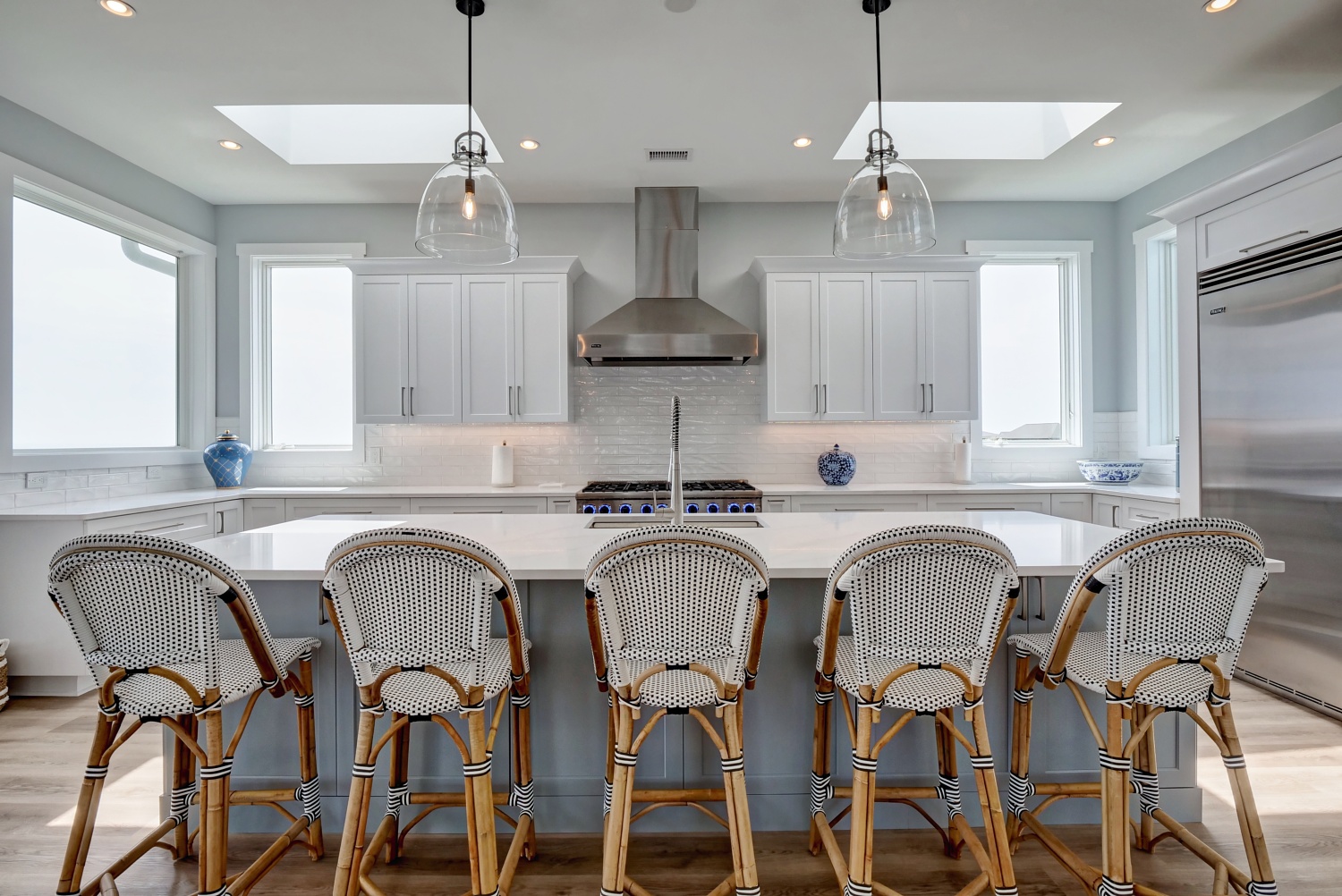 White Beach House kitchen with woven counter stools and glass pendant lights
